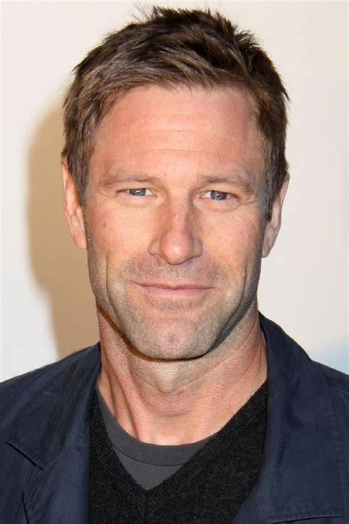 Aaron Eckhart smiling while wearing a blue suit.