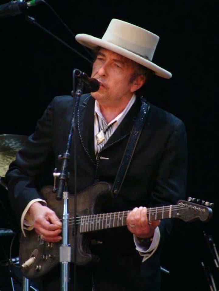 Bob Dylan wears a bolo tie and stands in front of a microphone.