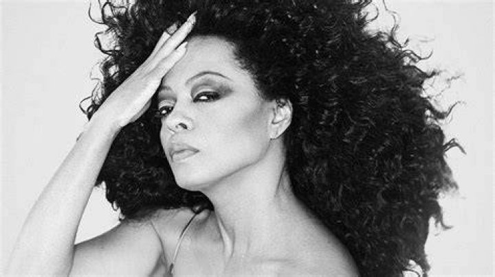 Diana Ross wears a bright red dress while performing in front of a purple backdrop onstage.