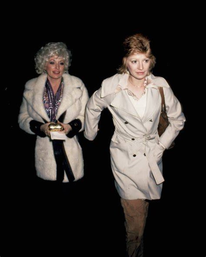 Dolly Parton and Judy Ogle wear tan coats and walk outside at night.