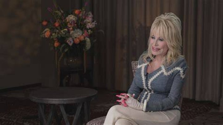 Dolly Parton sits in a rocking chair as she speaks into a microphone.