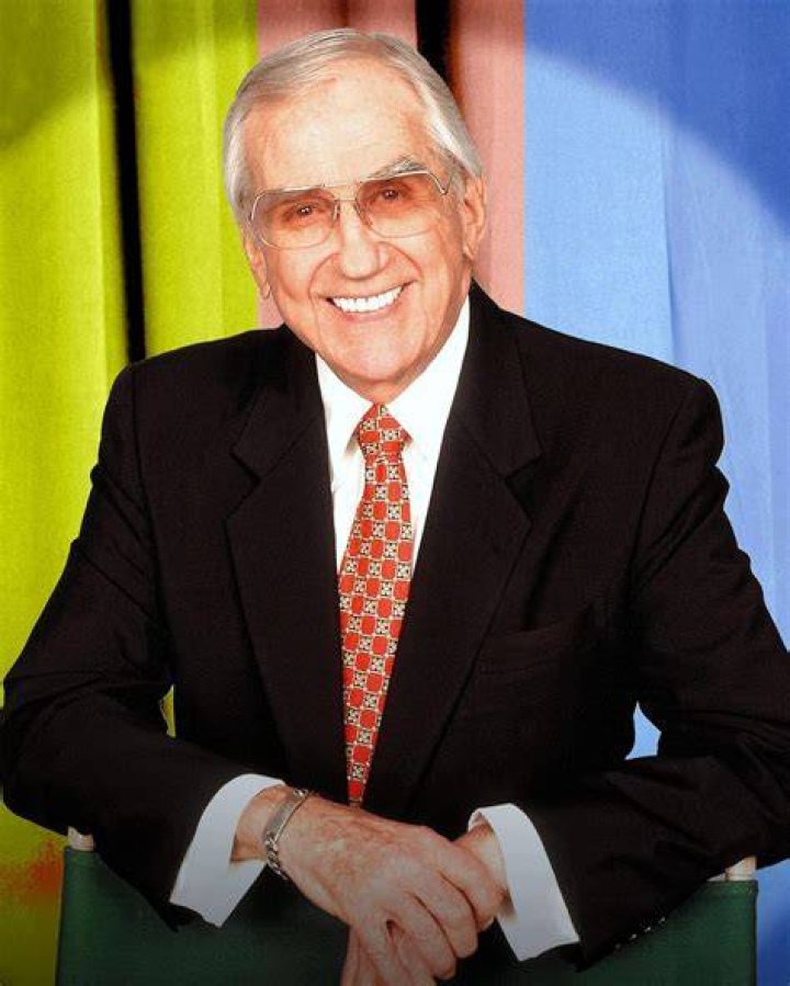 Ed McMahon in a pink shirt and tie with a dark blue jacket and Johnny Carson in a white button down shirt, both sitting on a couch c. 1985