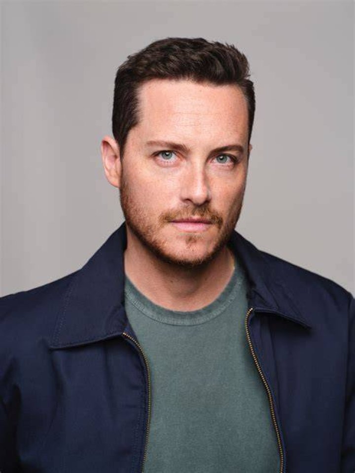 Jesse Lee Soffer posing in front of a gray curtain and a wooden ladder