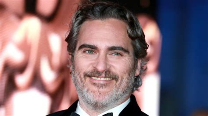 Joaquin Phoenix smiling at the Golden Globes while wearing sunglasses.