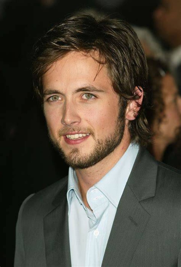 Justin Chatwin smiling in front of a red background