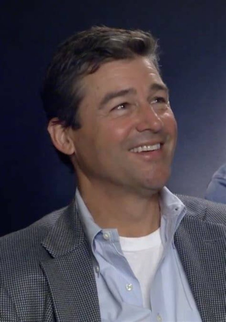Kyle Chandler in a black suit, standing next to Connie Britton in a red and white dress, each putting a hand on the other's shoulder