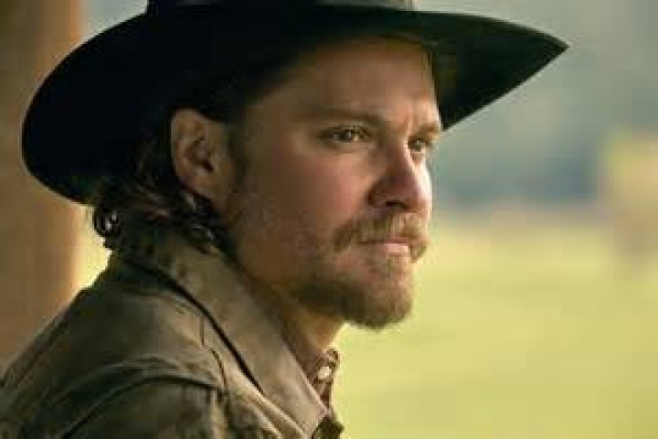 Luke Grimes as Kayce Dutton in Yellowstone. Kayce sits at his desk wearing a cowboy hat.