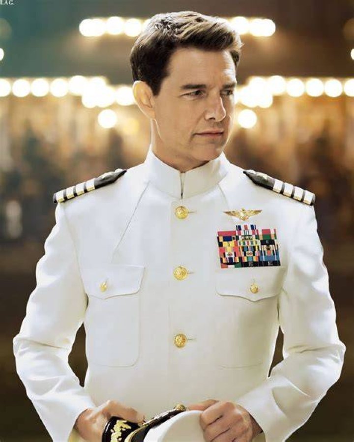 Tom Cruise in a navy suit, smiling at the camera